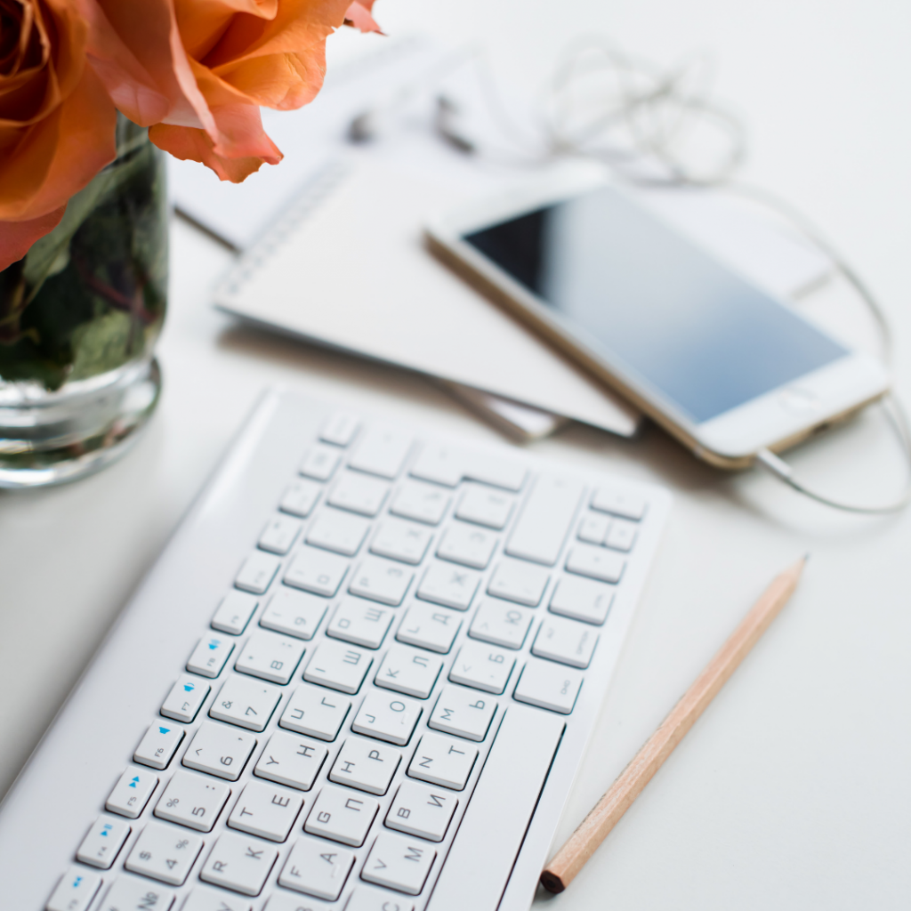 keyboard sitting next to flowers, a pencil and an iphone